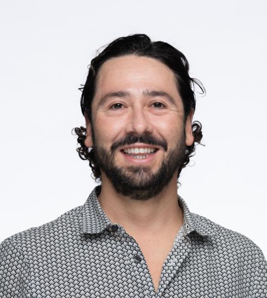 Headshot of smiling bearded man with gray patterned shirt on white background